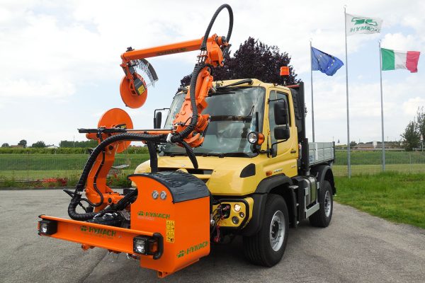 Macchina decespugliatrice scavallante ROAD-EAGLE MAXI UF Hymach per Unimog per sfalcio dell’erba attorno ai supporti del guard-rail lungo la strada.